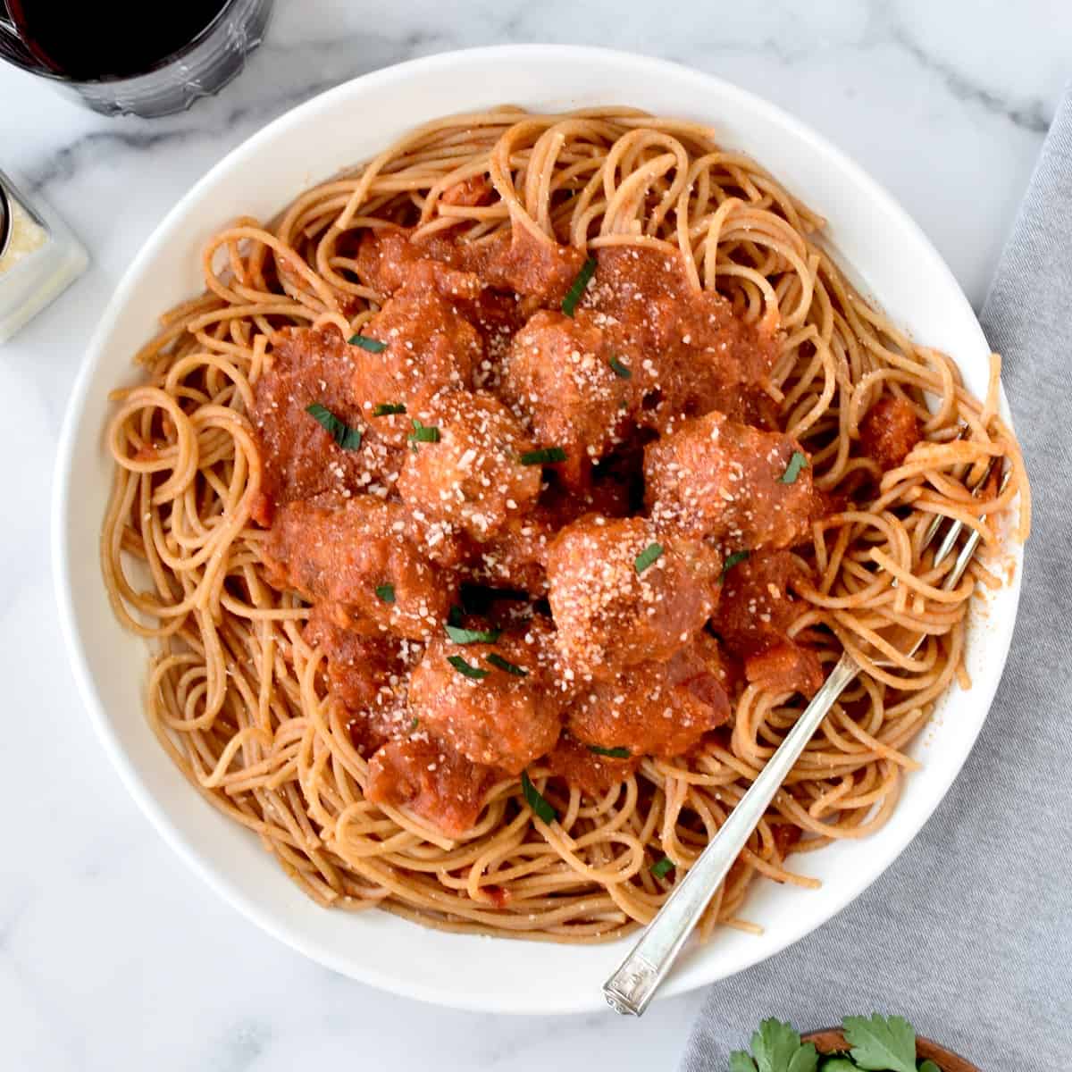 A white bowl with spaghetti noodles topped with turkey meatballs in marinara sauce. A fork is to the side with noodles twirled around it.