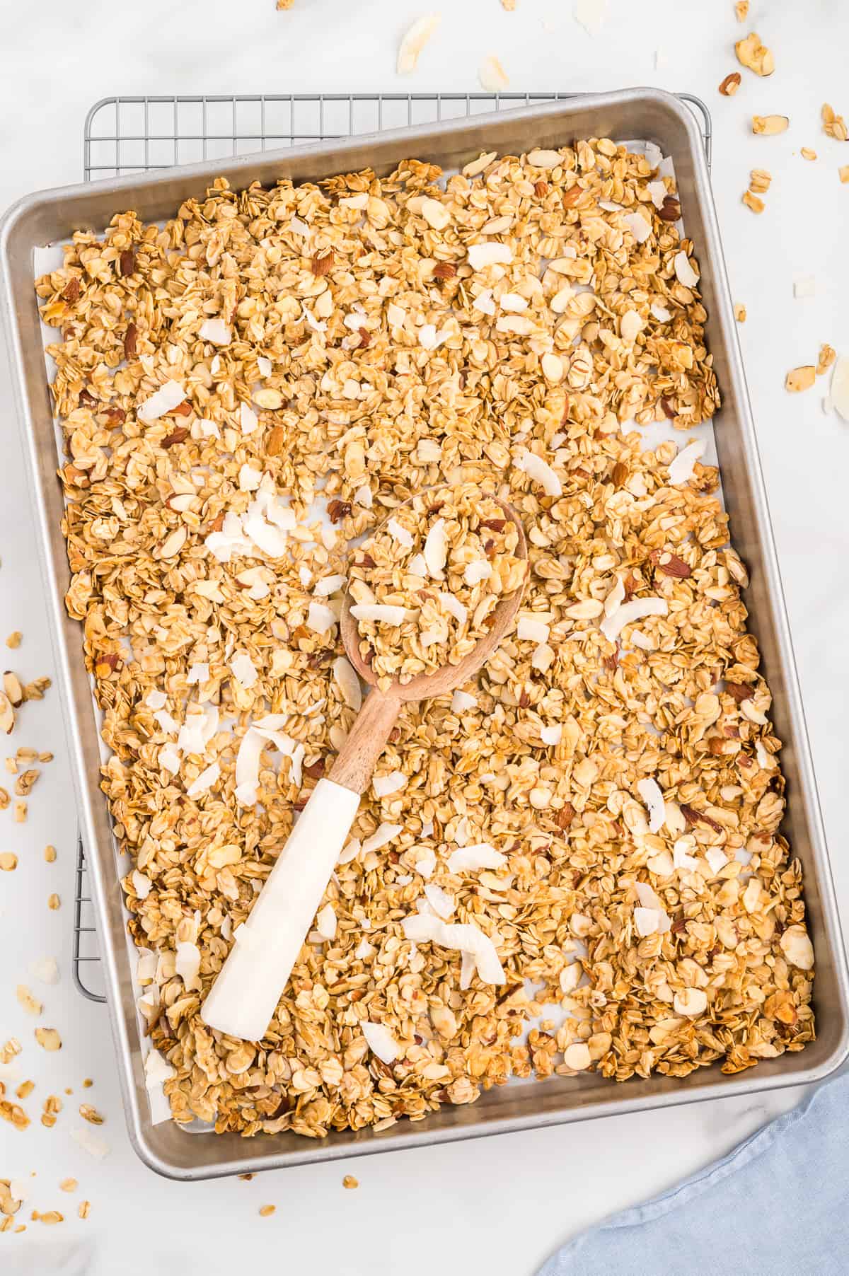 A sheet pan of vanilla almond granola garnished with coconut flakes, with some granola sprinkled around the pan on a marble background.